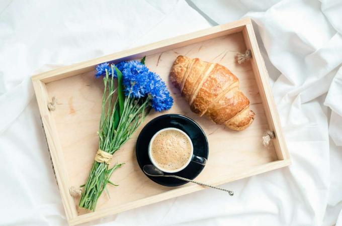Blåklint på en frukostbräda bredvid en croissant och kaffe