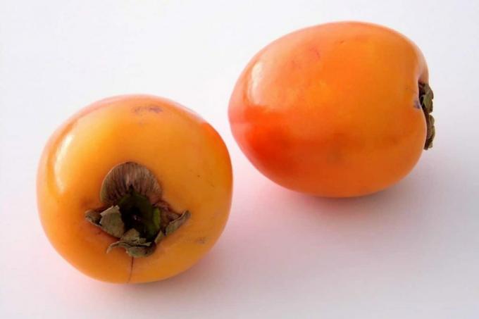 Billede af to persimmons med skræl og blade. Skrællen indeholder bitterstoffer.