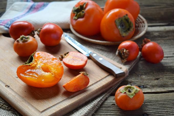 Persimmons skärs upp på en skärbräda med en kniv och persimmons i en skål